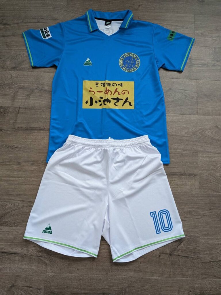 水色のサッカーユニフォームの前面と白のパンツ。胸に黄色のスポンサー、パンツに背番号10